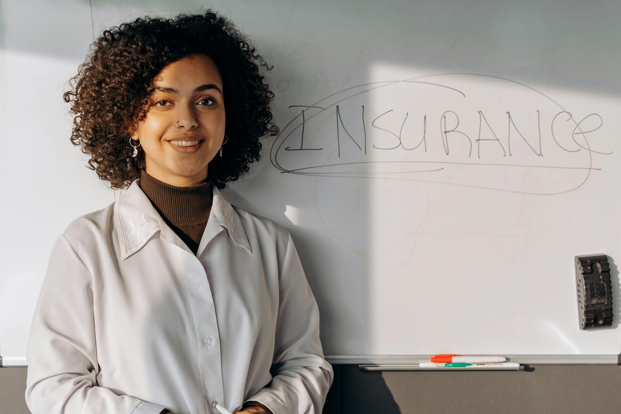 Woman standing in front of a white board that says, "Insurance". It is the featured image on a post about public liability insurance.